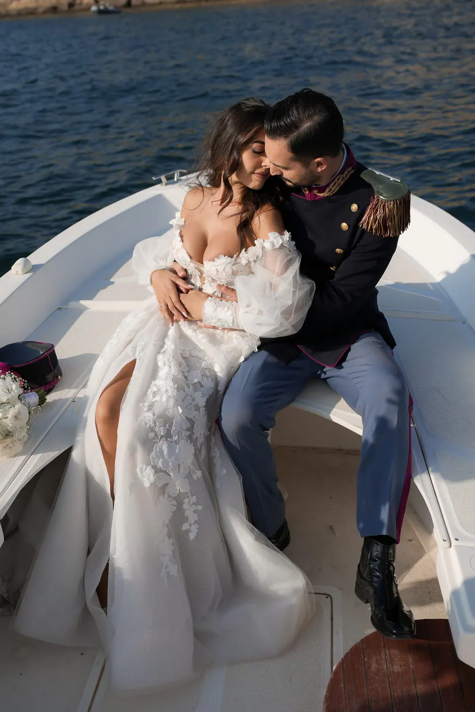 Bride and groom sitting on the bow of a boat, the dark blue sea around them.