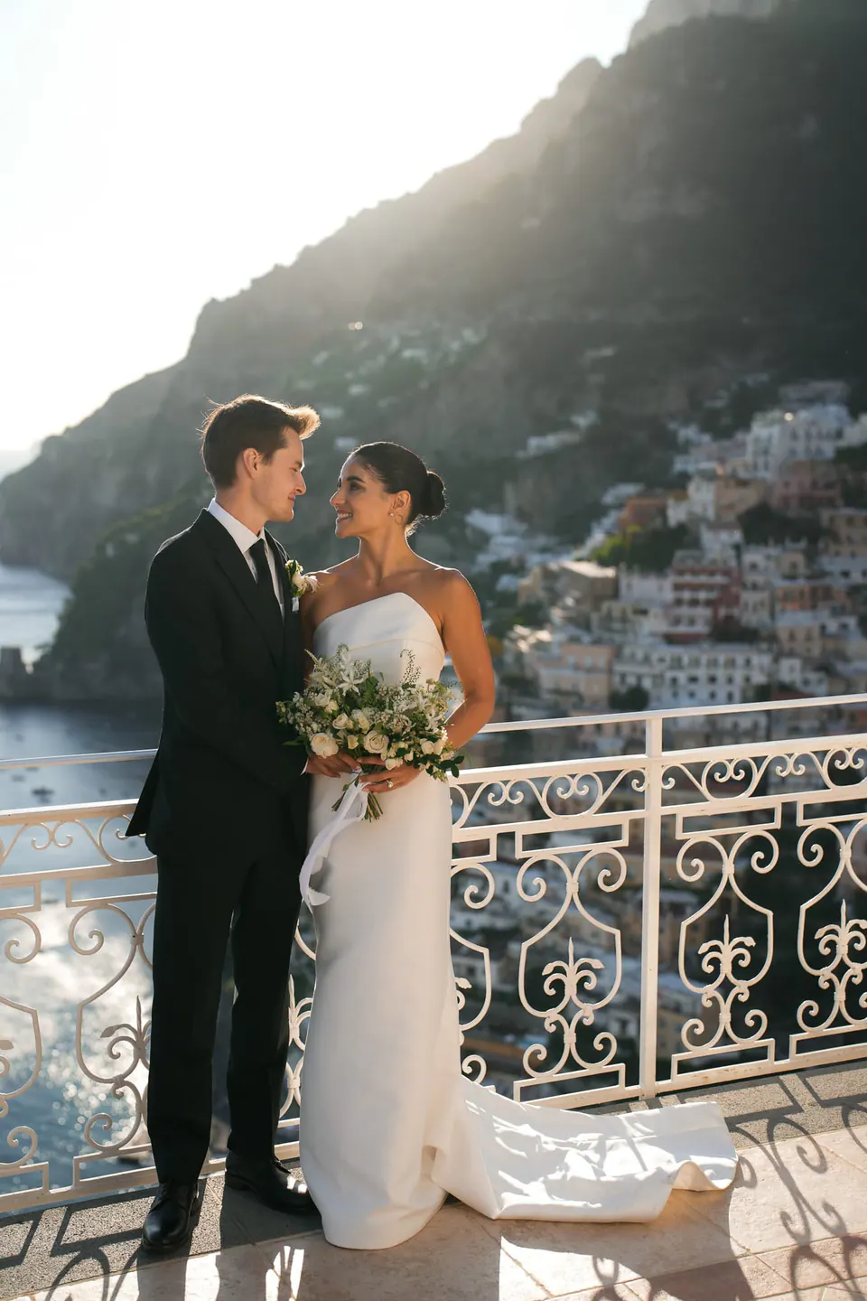 Bride and groom at the railing of the terrace, Positano behind them.