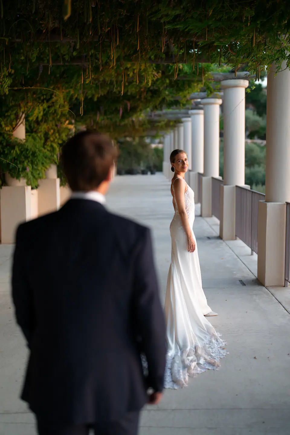 Groom watching the bride under a long colonnade.