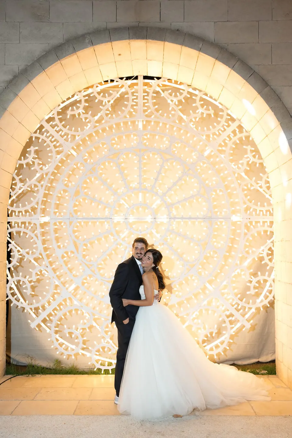 Bride and groom kissing under the illuminated carved stone arch at Tenuta San Domenico