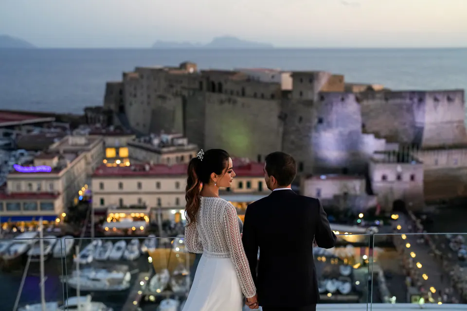 Bride and groom on the rooftop of Hotel Vesuvio at dusk, Castel dell'Ovo and the harbour below.