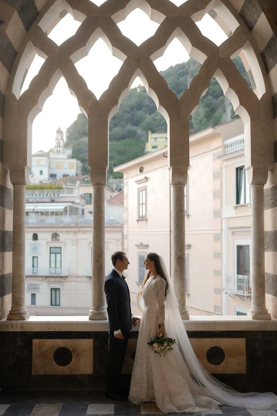 Bride and groom framed by an interlaced Gothic window, the town beyond.