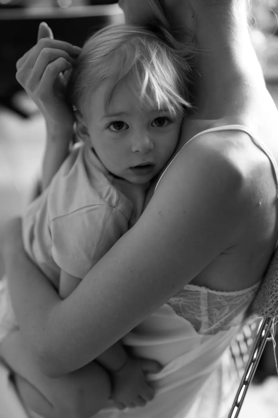 Primo piano in bianco e nero di un bambino appoggiato sulla spalla di una donna durante la mattina.