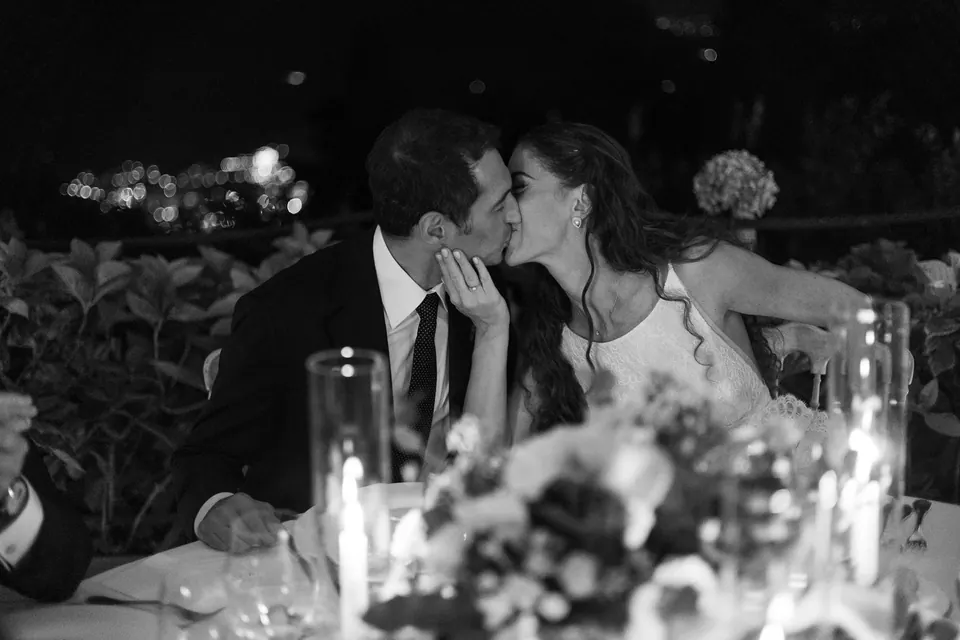 Black and white photo of the bride and groom kissing at the dinner table.