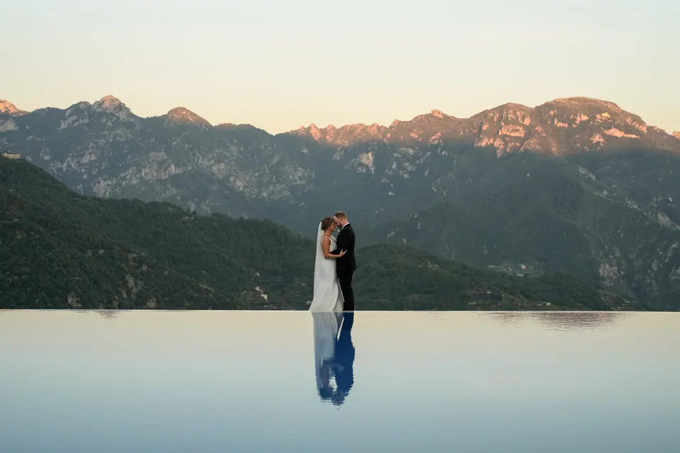 Bride and groom at the edge of the infinity pool, the mountains reflected in the water