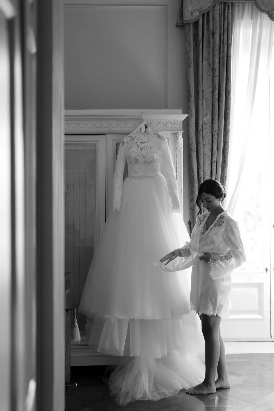 Black and white photo of the bride next to her hanging wedding dress