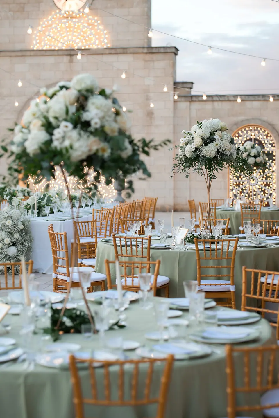 Reception tables with white linens, candles and flower centrepieces in the courtyard