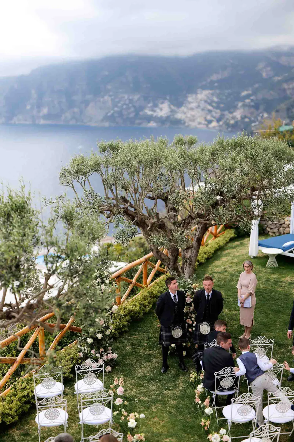 La cerimonia sul prato vista dall'alto, gli invitati tra gli ulivi con la costa alle spalle.