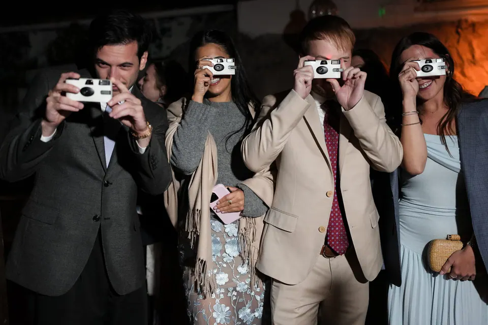 Guests photographing the couple with disposable cameras at the party.