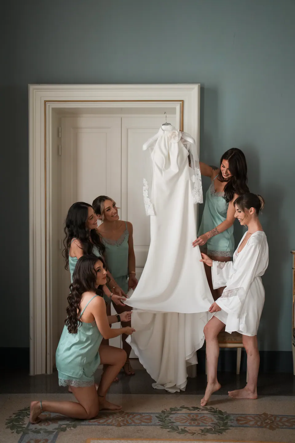 Le damigelle raccolte intorno all'abito appeso alla porta, mentre aiutano la sposa.