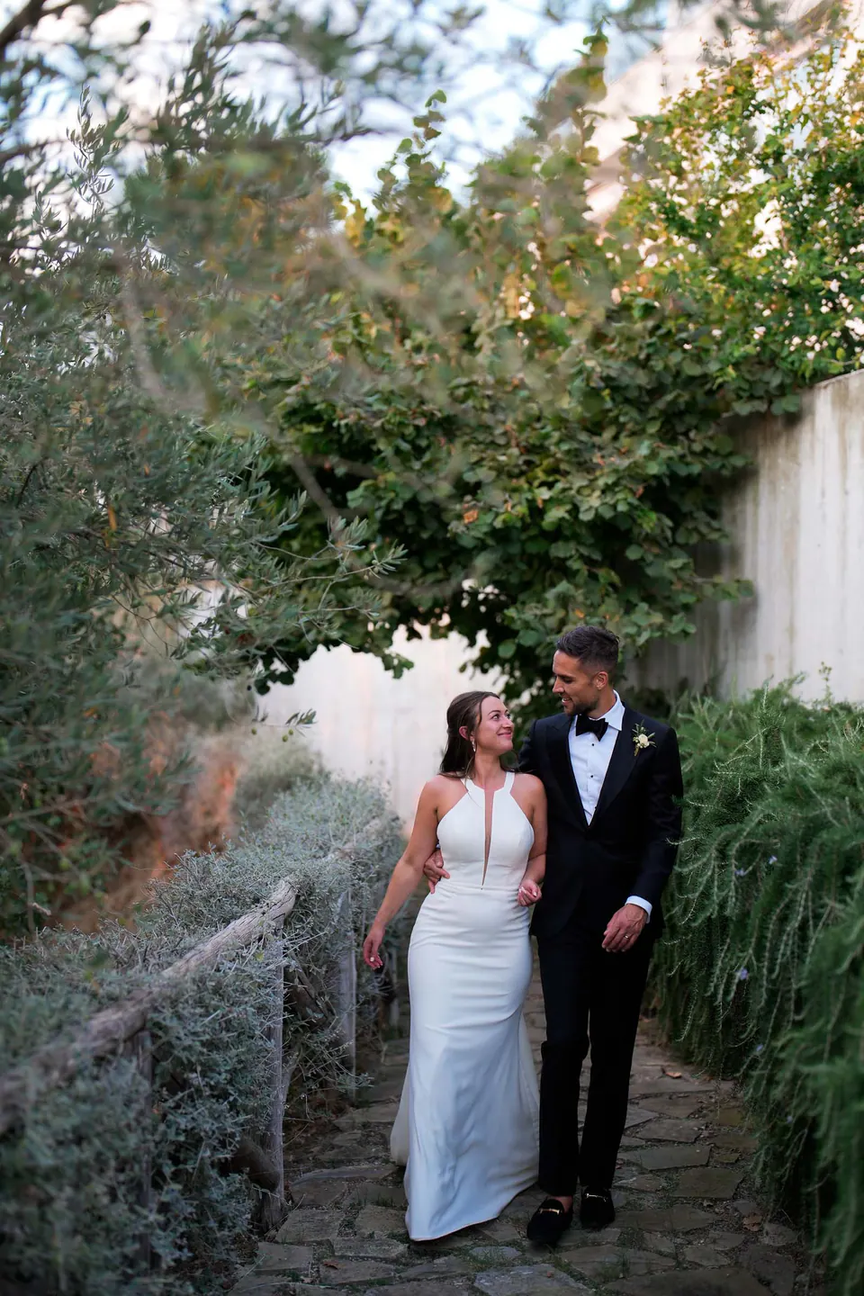 Couple walking along the villa pathway framed by trees, peaceful and romantic wedding stroll.