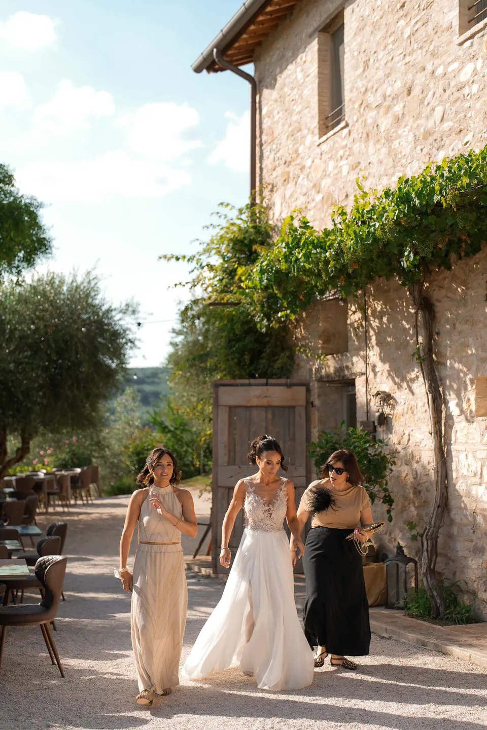 Bride walking with two women beside the stone farmhouse