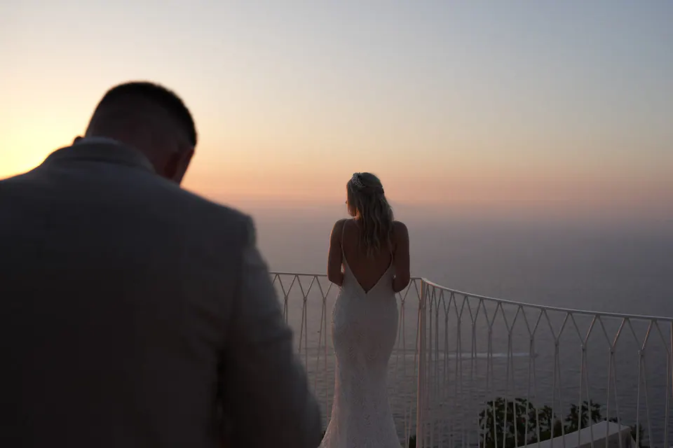 Lo sposo che vede la sposa di spalle alla ringhiera al tramonto