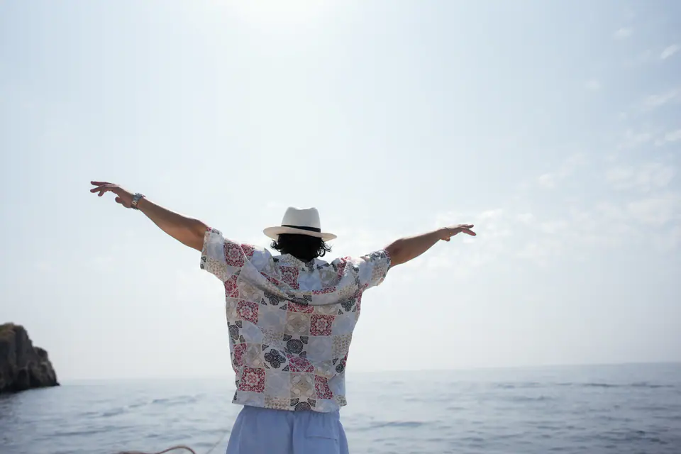 A friend with arms wide open at the bow of the boat, the sea ahead.