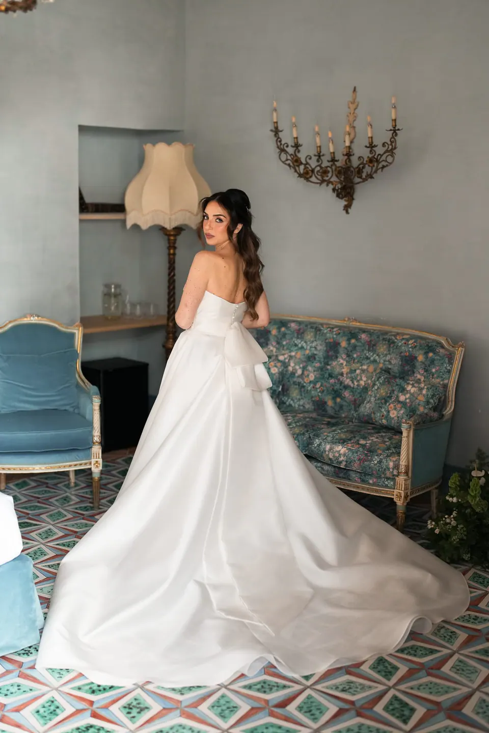 Bride in her gown seen from behind in a room with floral sofas