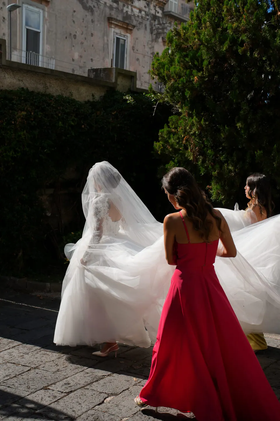 A guest in red holding the bride's long veil outdoors