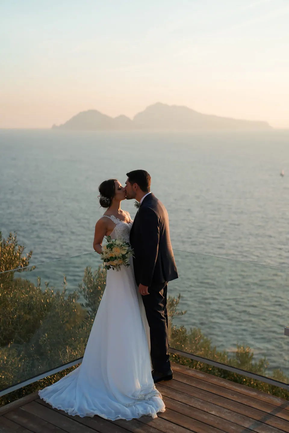 Bride and groom kissing on the terrace at sunset, Capri on the horizon.