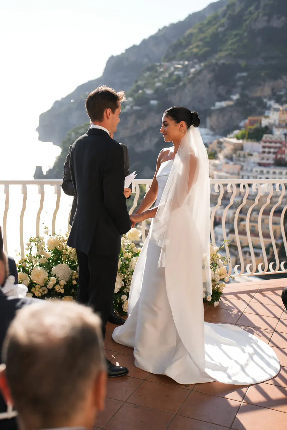 Bride and groom holding hands at the altar, a guest in the foreground.