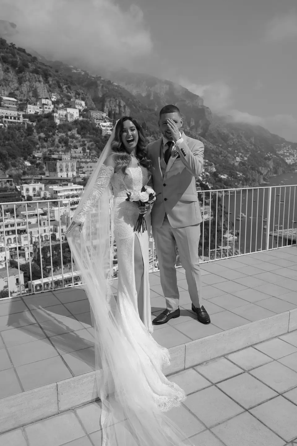 Black and white portrait of the couple on the terrace, Positano and the sea behind.