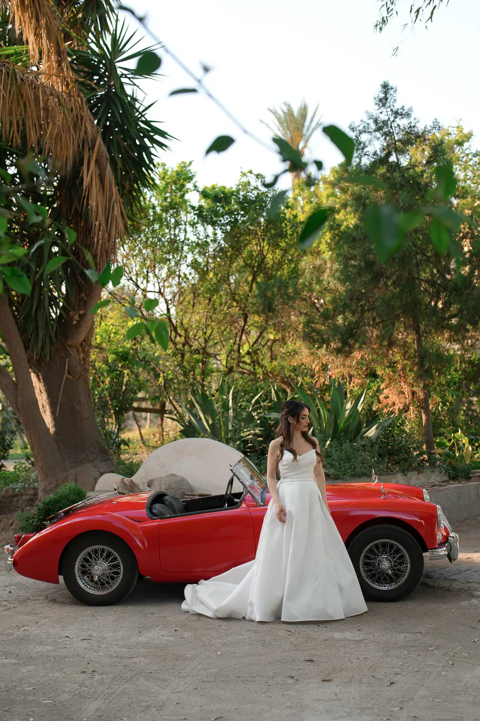 Alessandra con su vestido de novia junto a un coche antiguo rojo.
