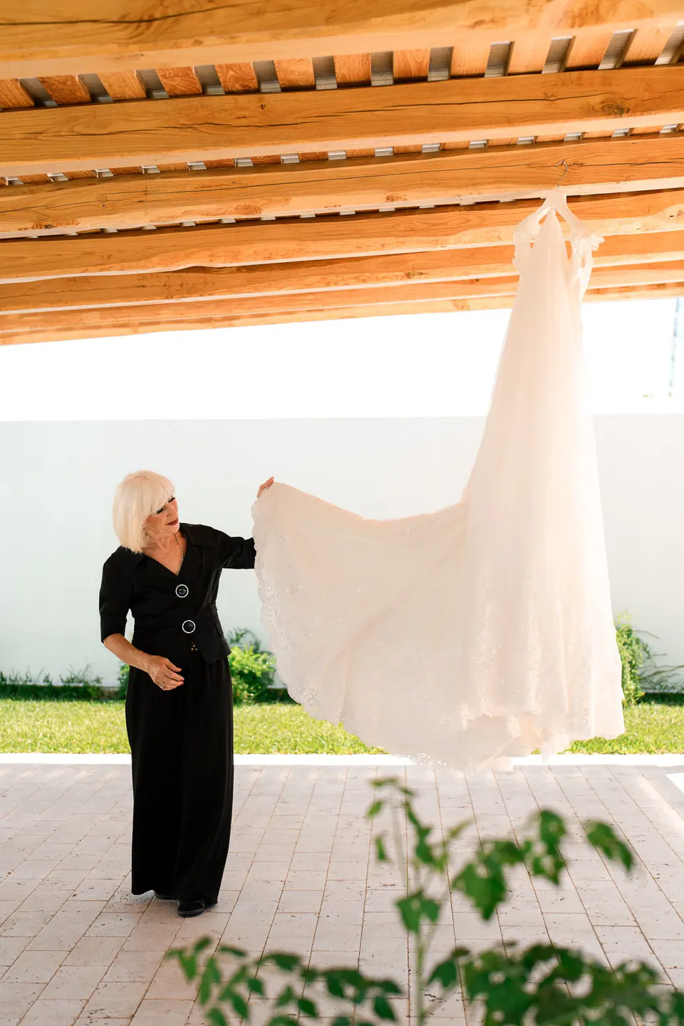 A woman holding up the wedding dress under a wooden pergola
