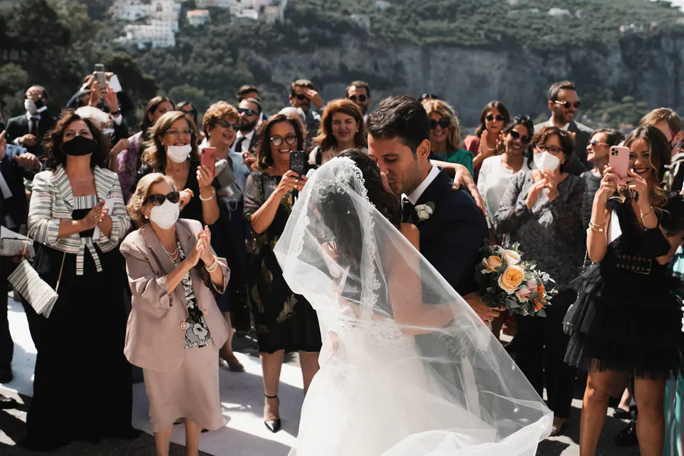 Sposi che attraversano gli invitati in festa dopo la cerimonia, il velo che vola.