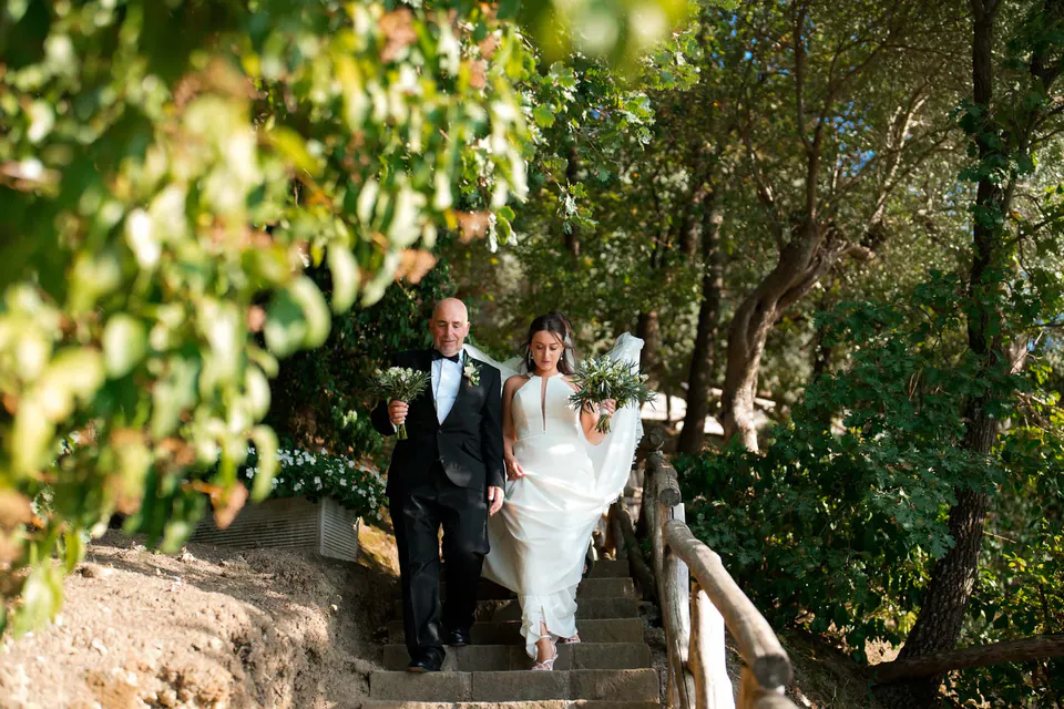 Bride and groom walking down a wooded garden path in the evening light.