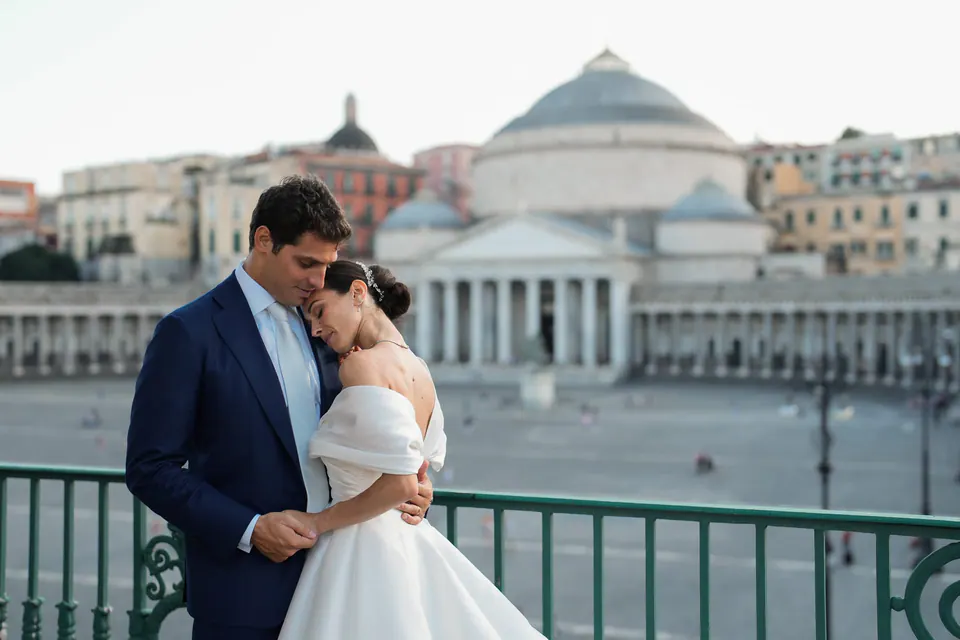 Sposi abbracciati su un balcone, la cupola di San Francesco di Paola alle spalle.