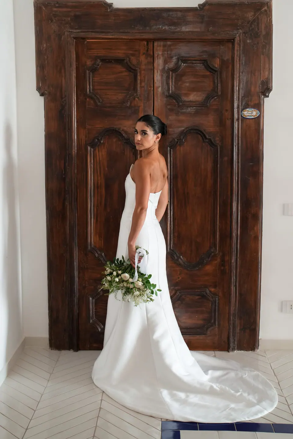 Bride standing in front of a carved wooden door, her train spread on the floor.