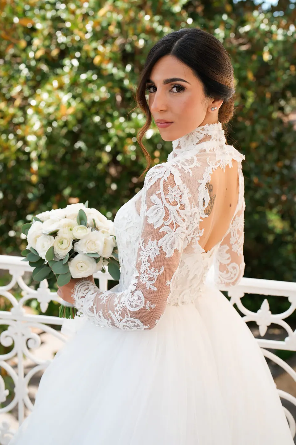 Bride in lace gown leaning on the villa balcony, radiant and serene during golden hour.