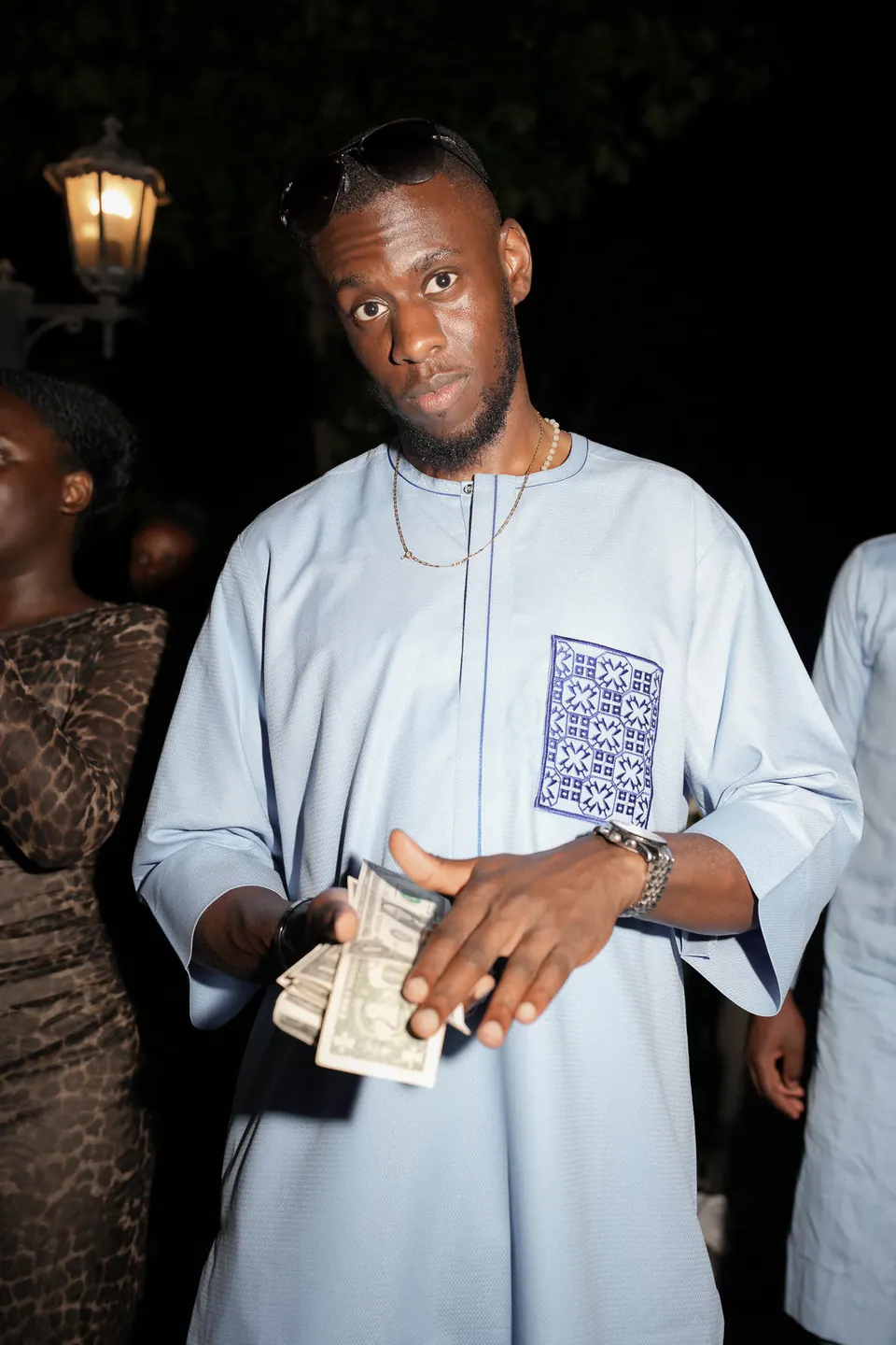 Una invitada con traje nigeriano azul claro sostiene billetes para el money spraying en el banquete.