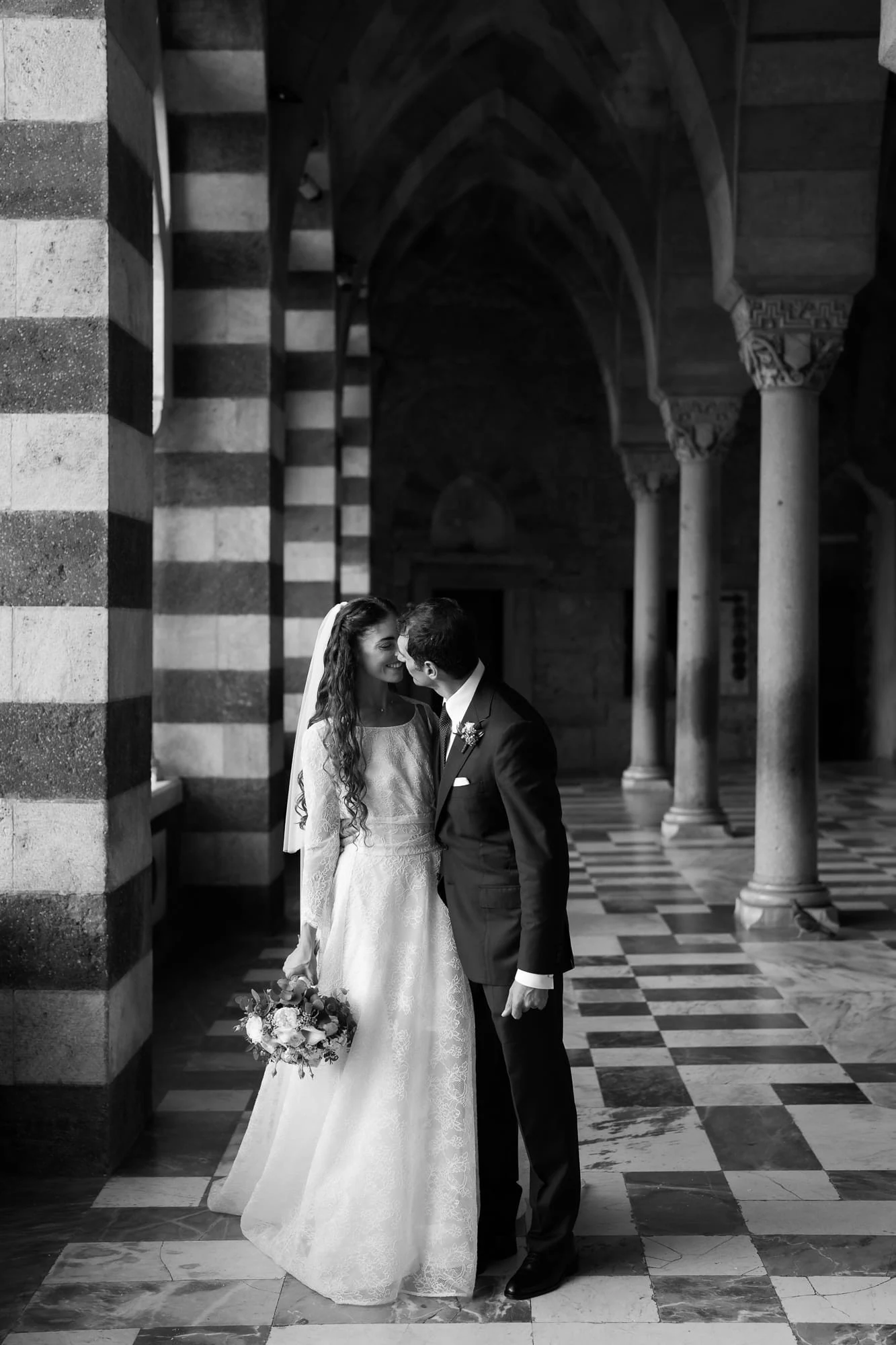 Schwarzweißfoto des Paares unter den gestreiften Bögen im Vorhof des Doms von Amalfi.