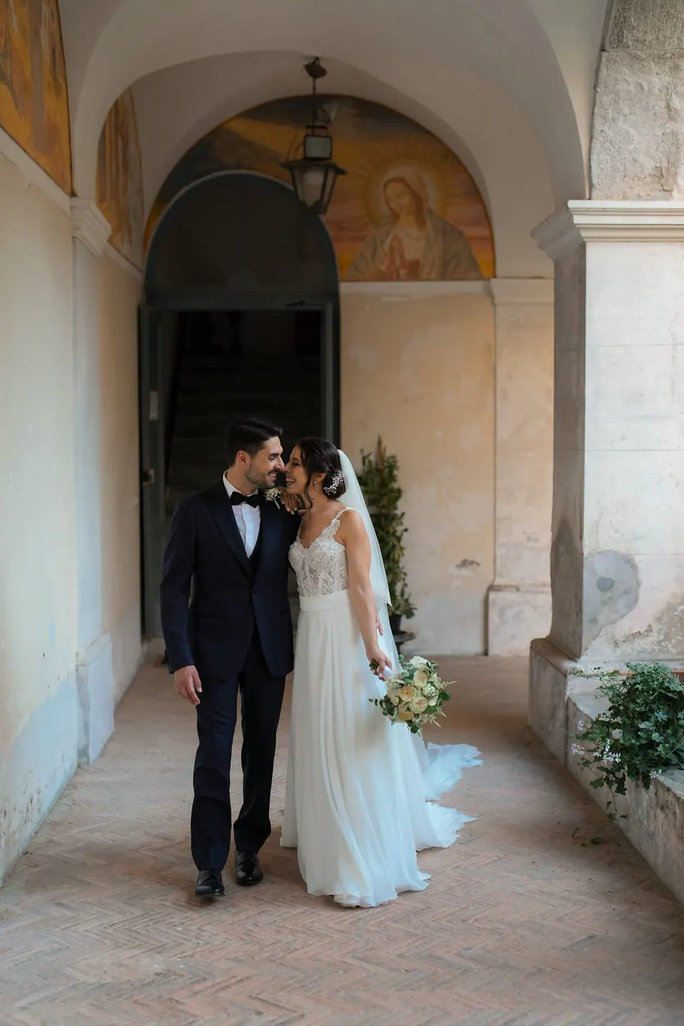 Bride and groom kissing beneath the frescoed arch of the cloister.