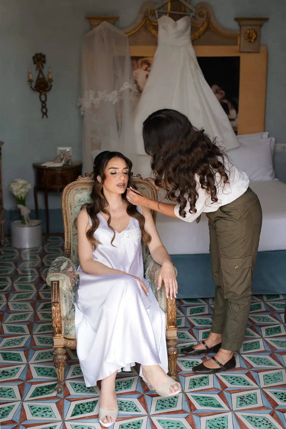 La novia con combinación sentada en un sillón, con el vestido colgado detrás.