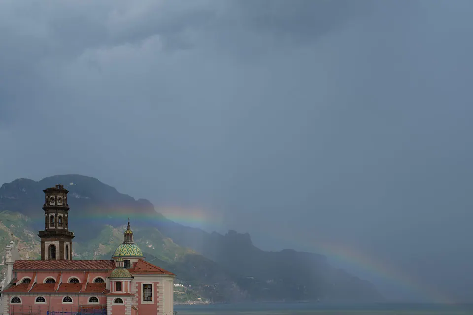 Ein Regenbogen über einer Kirche und den Dächern der Küste unter Gewitterhimmel.