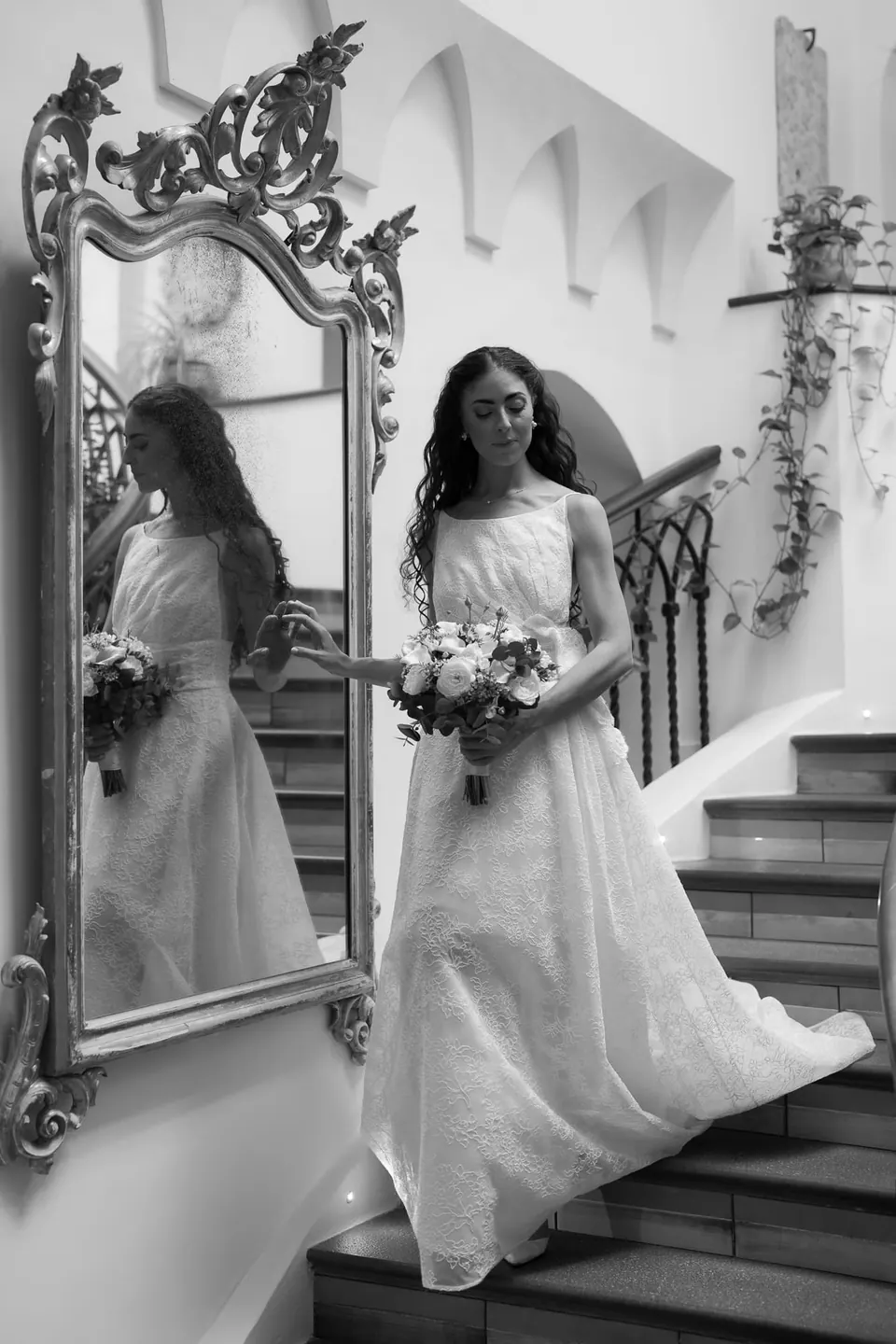 Black and white photo of the bride on the staircase, reflected in an ornate mirror.
