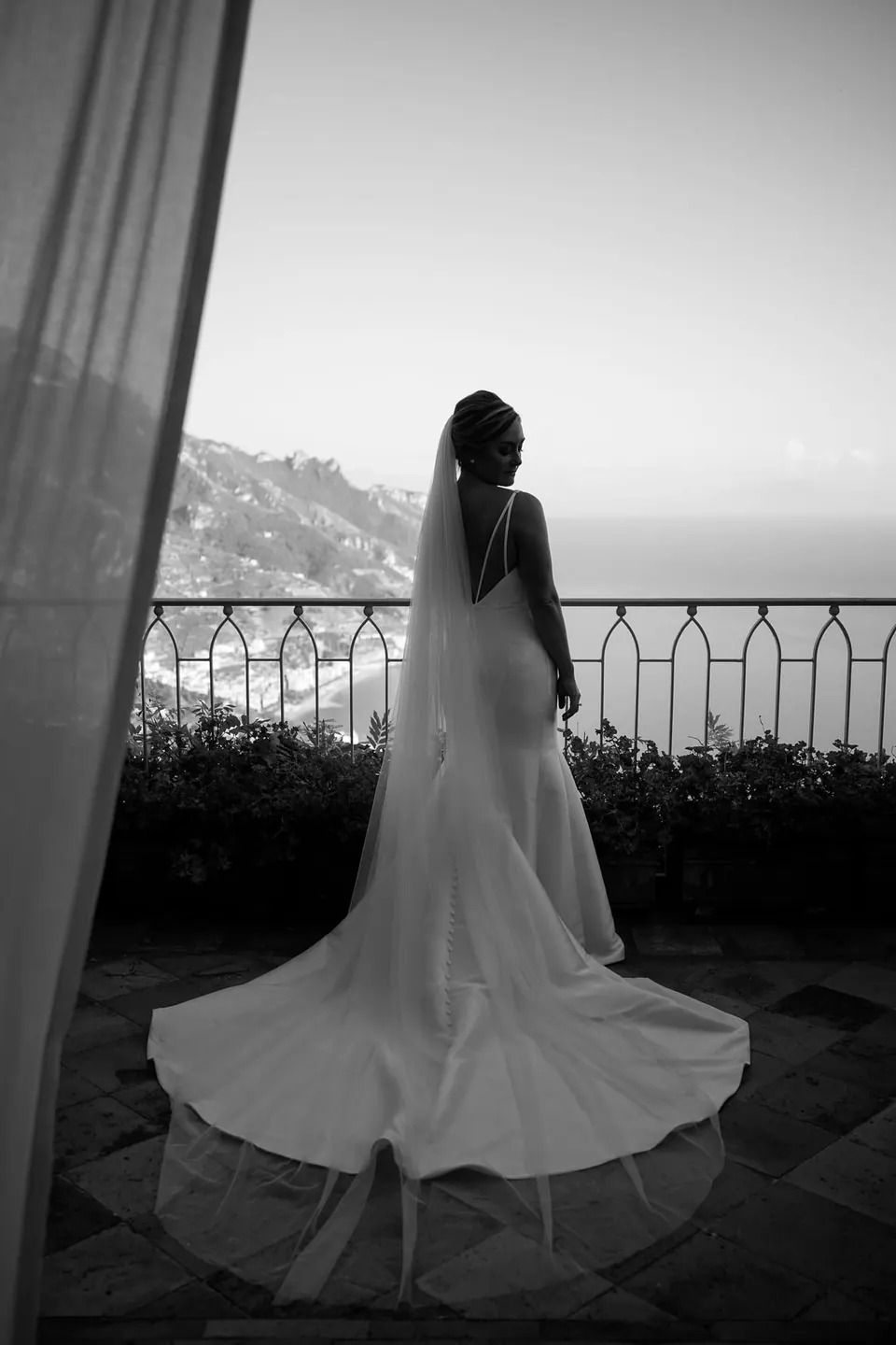 Black and white photo of the bride seen from behind at a terrace railing