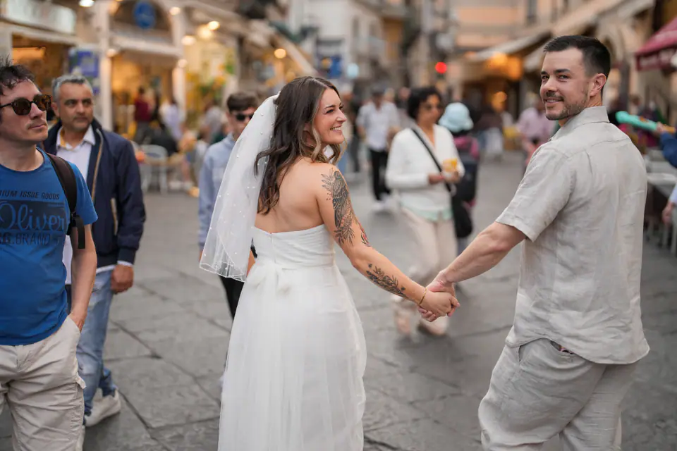 Bride leading the groom by the hand through the crowd in the main street of Amalfi.