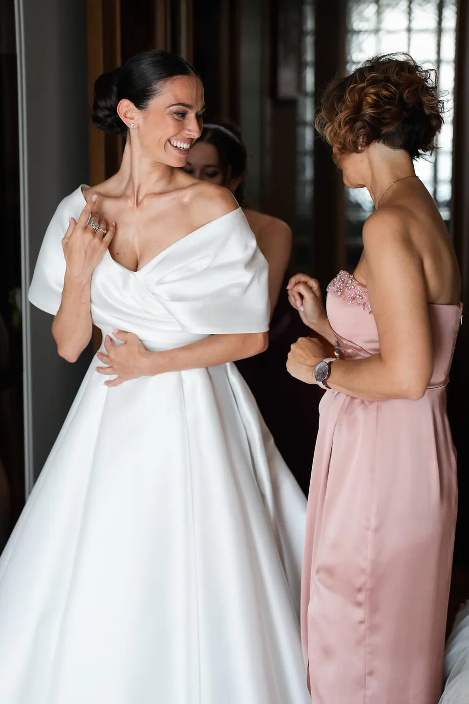 Sposa che ride con una damigella in abito rosa.