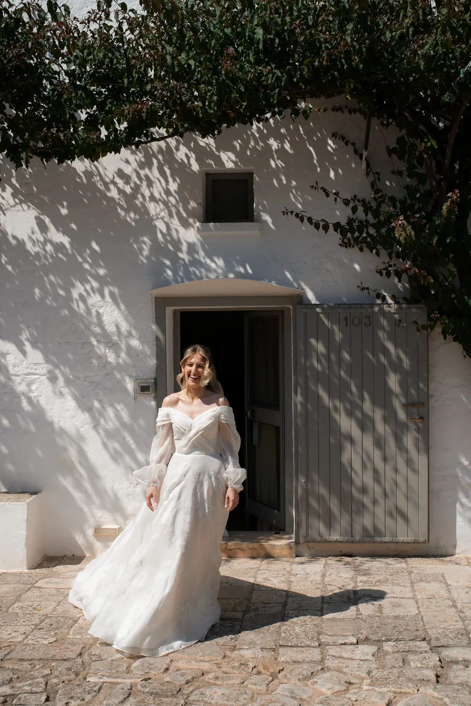 La novia sale al sol por la puerta de una casa encalada.