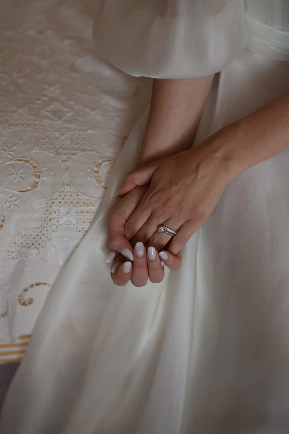 Nahaufnahme der Hände der Braut mit ihren Ringen auf der Seide des Kleides.
