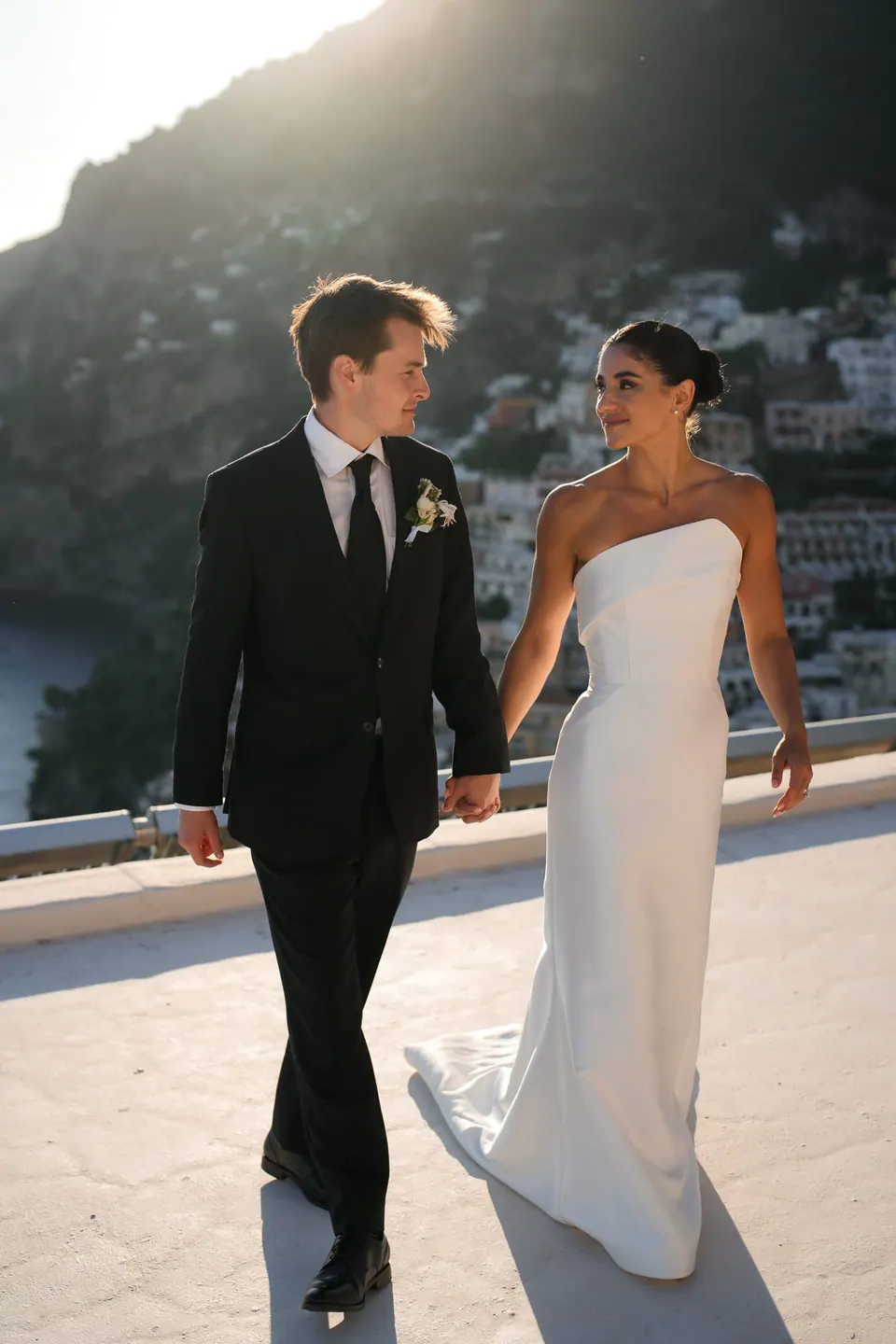 Bride and groom walking across the terrace in the late afternoon light.
