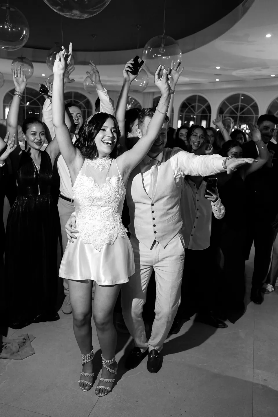 La mariée bras levés sur une piste bondée, en noir et blanc.