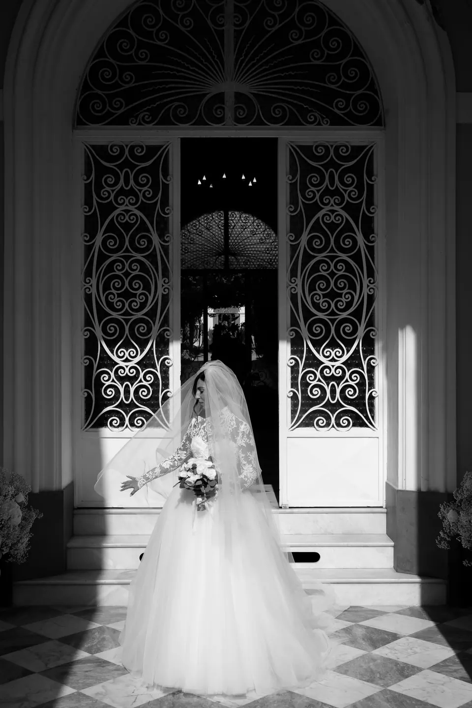 Black and white photo of the bride in a doorway with ornate iron doors