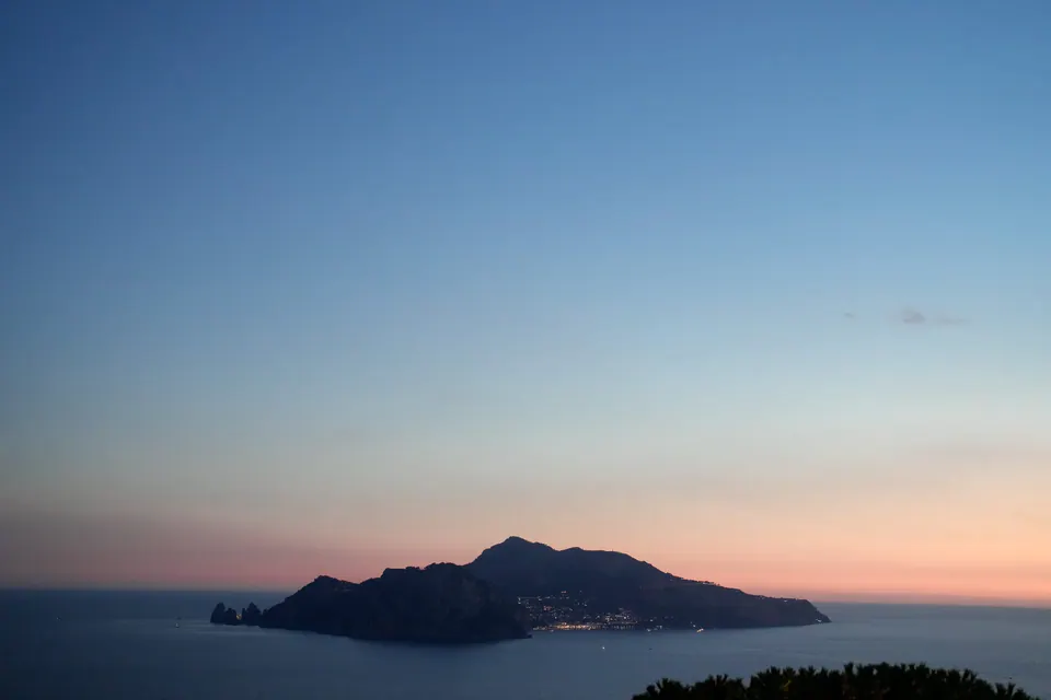Sunset over Capri island viewed from Relais Blu, pastel sky painting a romantic Mediterranean scene.
