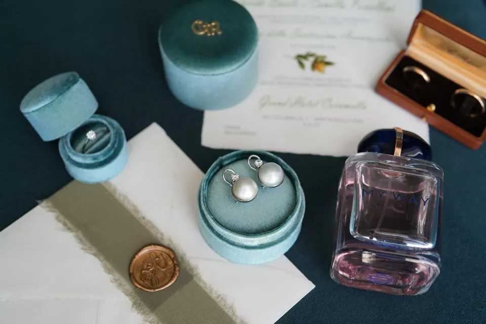 Flatlay mit Ringschachteln, Parfum, einer wachsversiegelten Einladung und einer Samtbox.