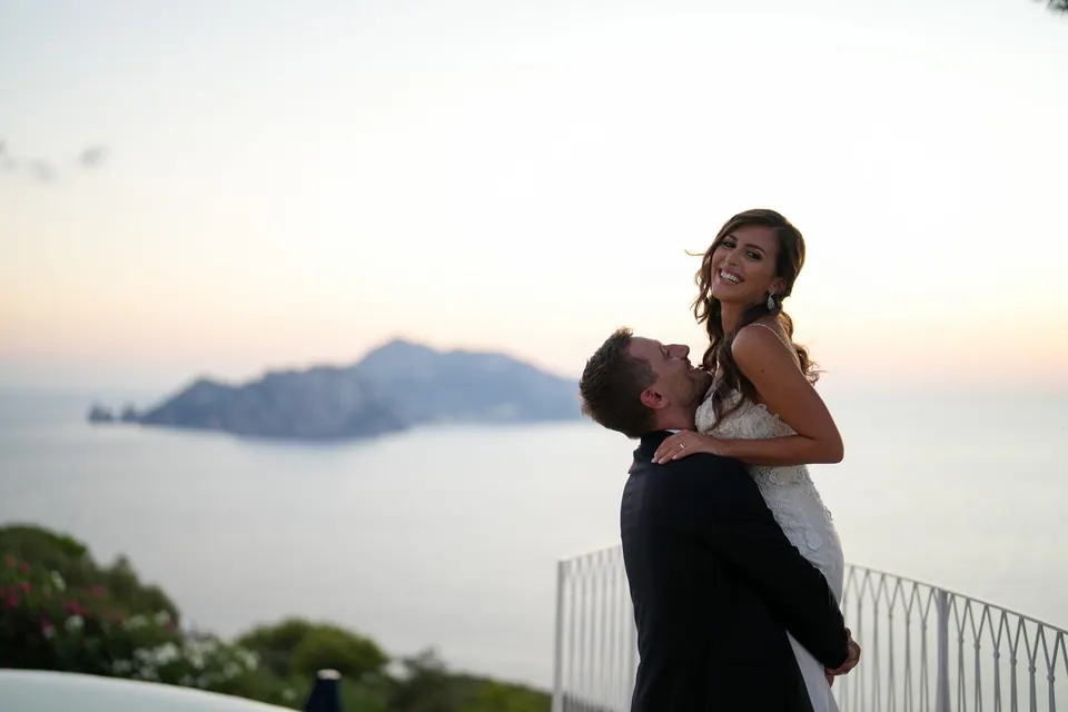 Lo sposo solleva la sposa al tramonto, Capri all'orizzonte.
