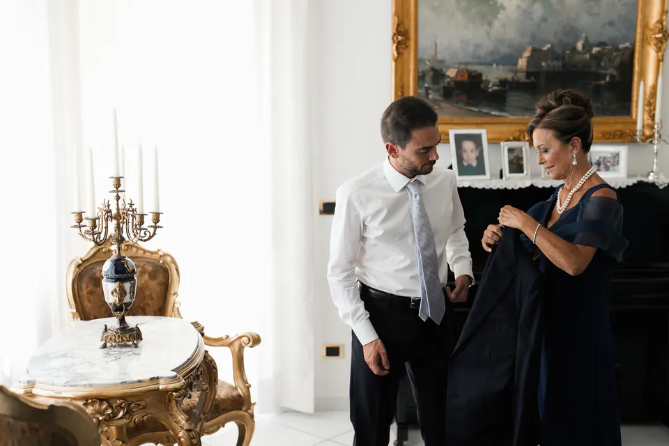 A woman adjusting the groom's tie in a room with gilded furniture.