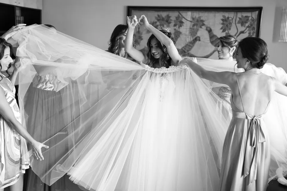 Foto in bianco e nero delle damigelle che sollevano il lungo velo sopra la sposa.