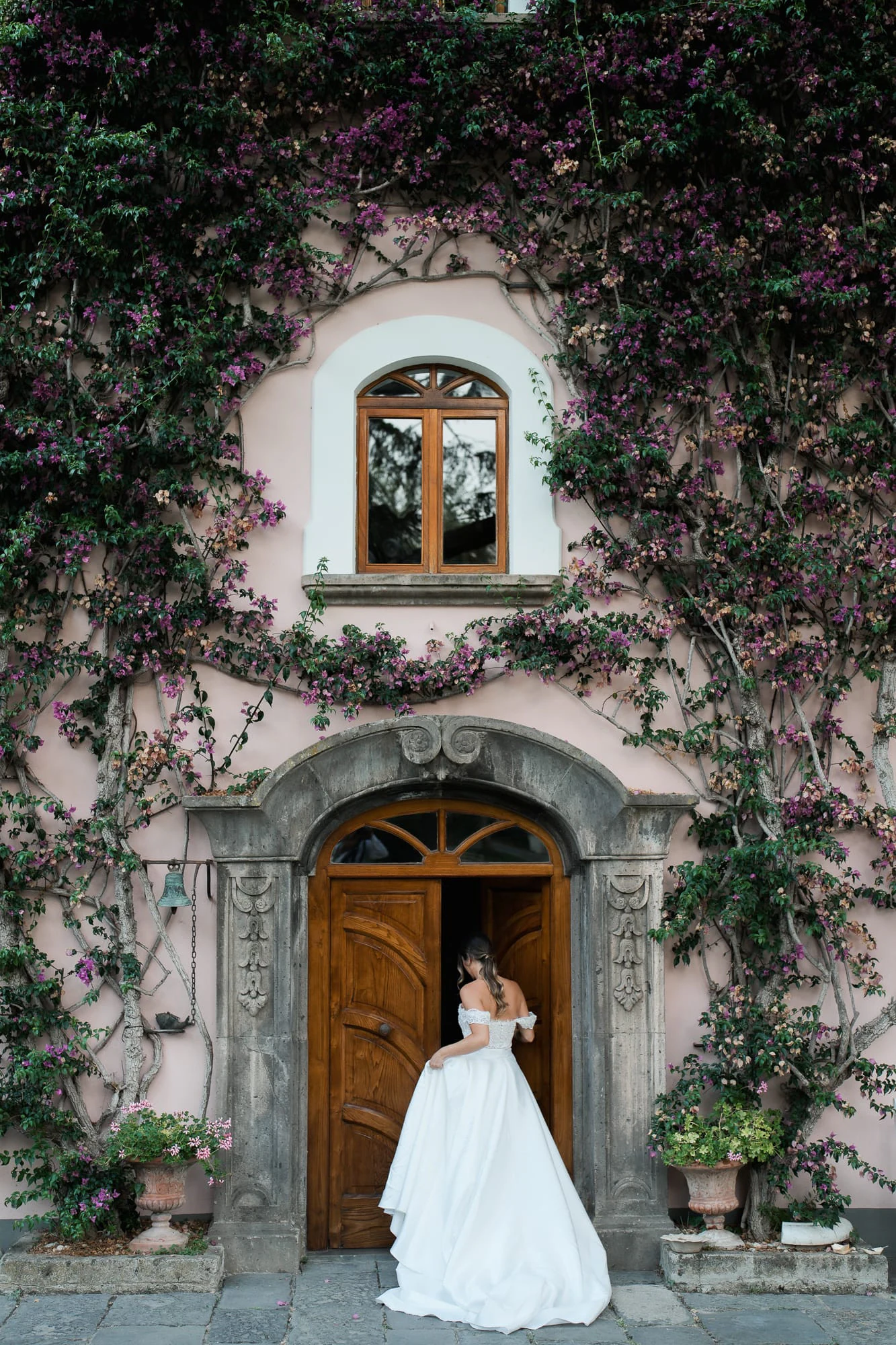 Bride at the arched wooden door of the pink, ivy-covered villa of Capo Santa Fortunata.